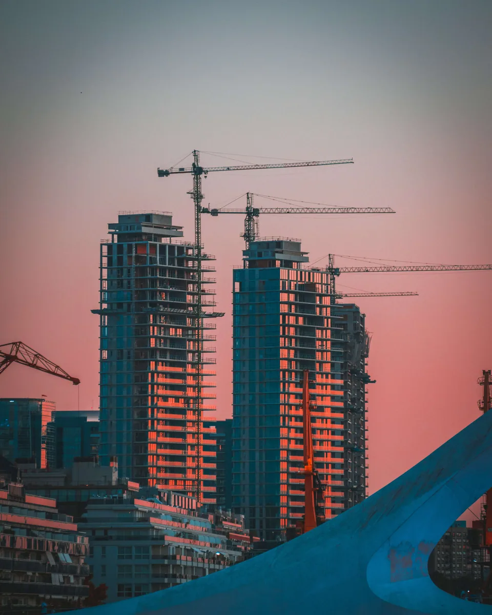 Sunset picture of two buildings in construction and a crane in the background.